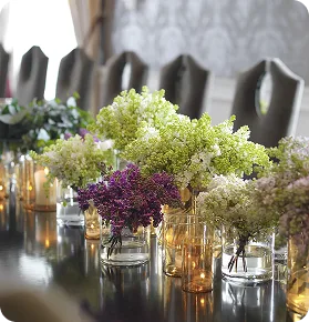 Blomsteroppsats med syrin og telys langs et festbord